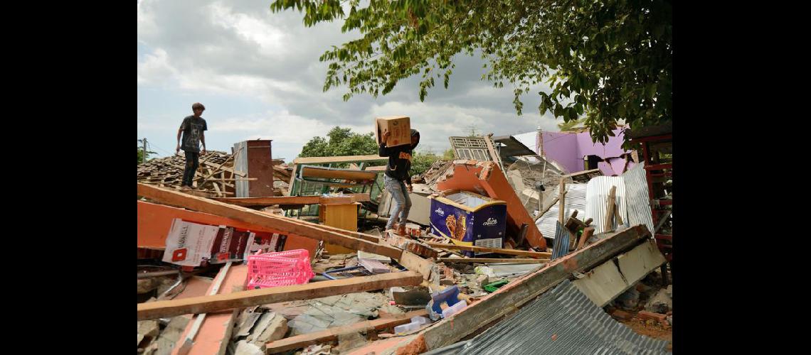  Un joven rescata sus pertenencias mientras trepa sobre los escombros de una casa derrumbada en Kayangan (NA)