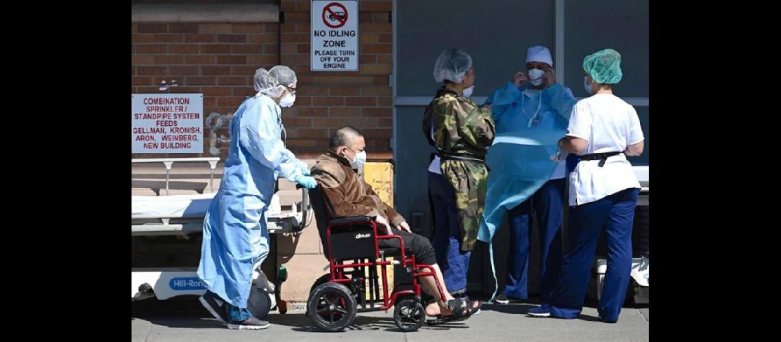  Un trabajador de la salud traslada a un paciente con coronavirus en una silla de ruedas en un hospital de la ciudad de Brooklyn en Nueva York  (AFP)